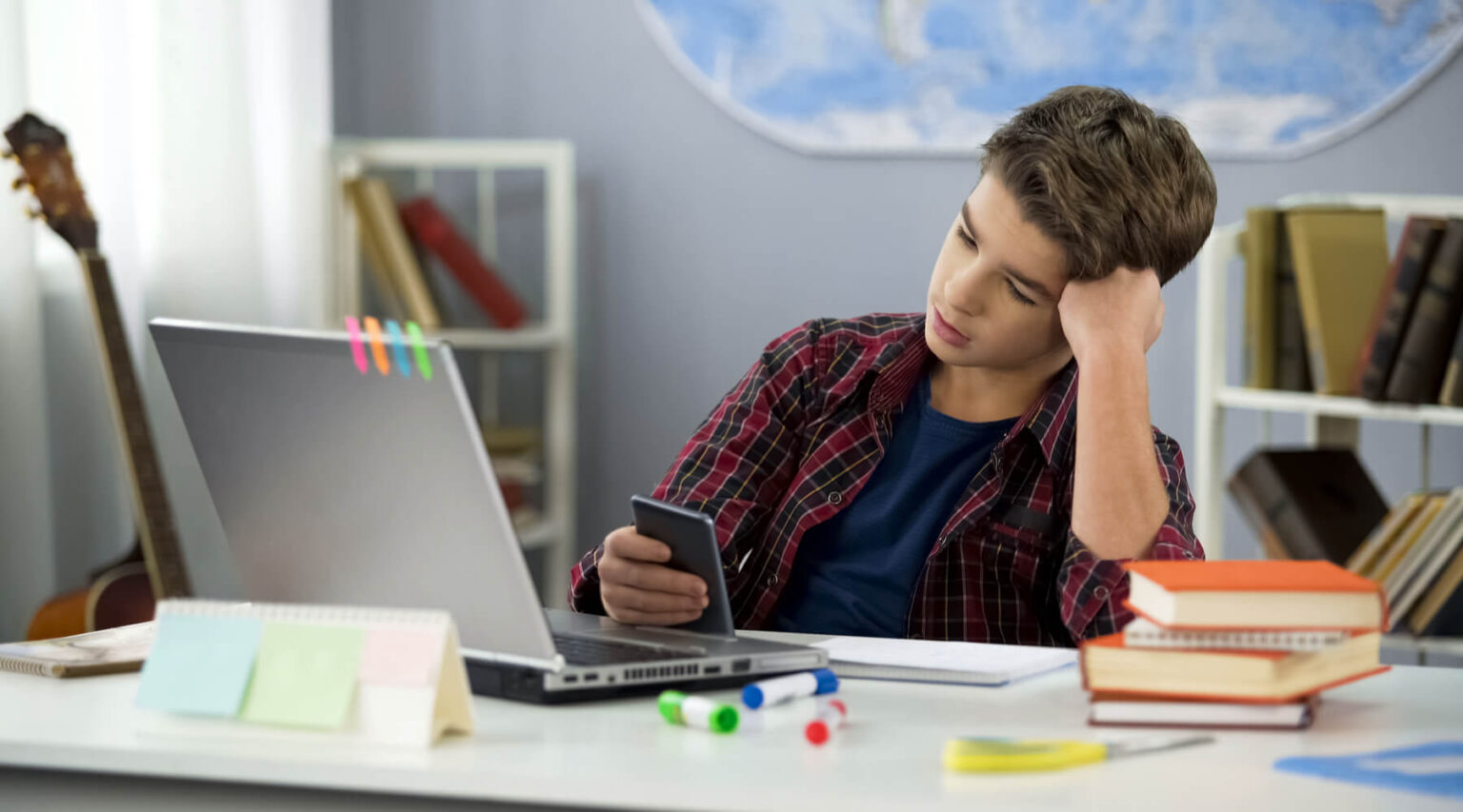 A boy sat behind his desk and watching his phone